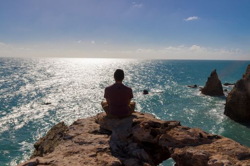 A male sitting on the rock looking at the blue shining sea under a clear sky