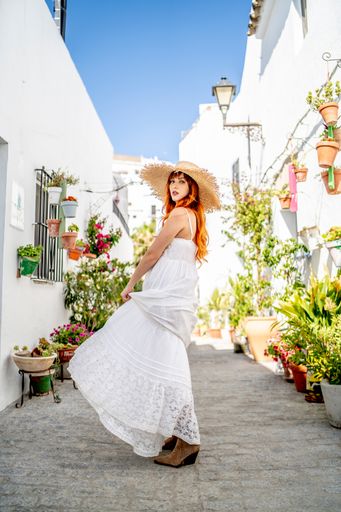 A beautiful redhead model from Spain in an elegant dress and a straw hat posing outdoors