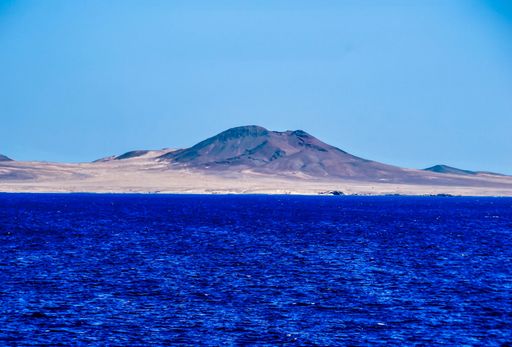 A breathtaking view of a mountain behind the beautiful calm ocean under the clear blue sky