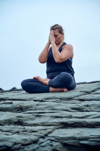 A vertical shot of a Native American woman from Spain practicing yoga on rocks on a gloomy day
