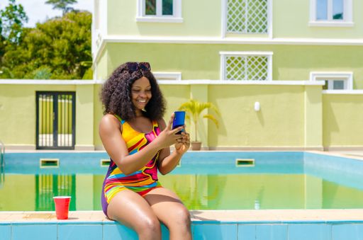 A cheerful young beautiful Nigerian female having fun by the pool and taking selfies