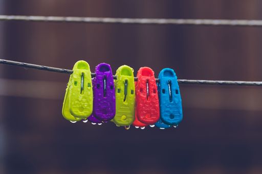 Colorful plastic clothespins with water droplets hanging on a wire against a blurred background.