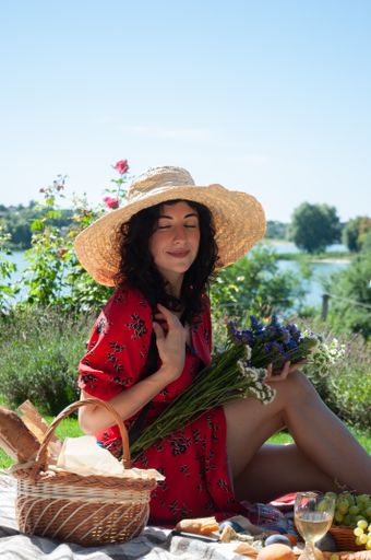 A vertical shot of a young Caucasian female in a red dress and straw hat having picnic on a sunny day