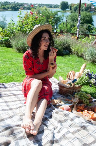 A vertical shot of a young Caucasian female in a red dress and straw hat having picnic on a sunny day