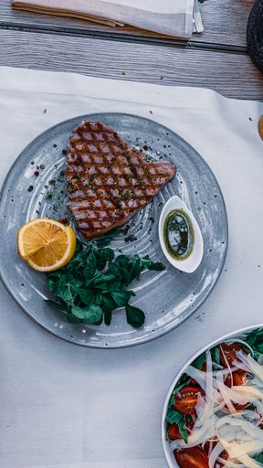 A top view shot of a plate with tuna steak, a sauce, greens, and a lemon on the side