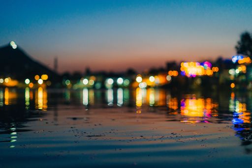A serene evening view of a waterfront with colorful bokeh lights reflecting on the water under a twilight sky.
