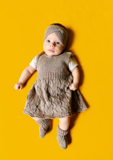 A vertical shot of a cute little Ukrainian baby girl in a brown dress with a her toy lying on a yellow background