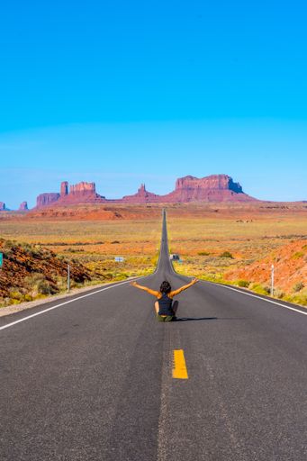 A vertical shot of a young female sitting in the middle of the road in Monument Valley, Utah, USA