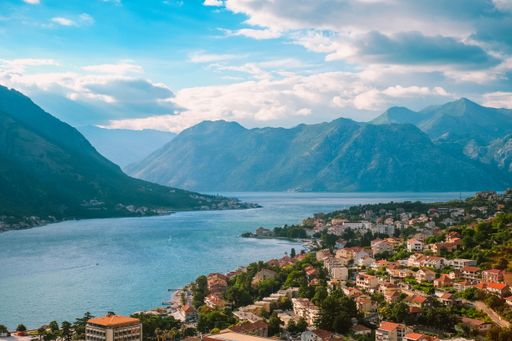 Scenic view of Kotor Bay with mountains and coastal town under a partly cloudy sky in Montenegro.
