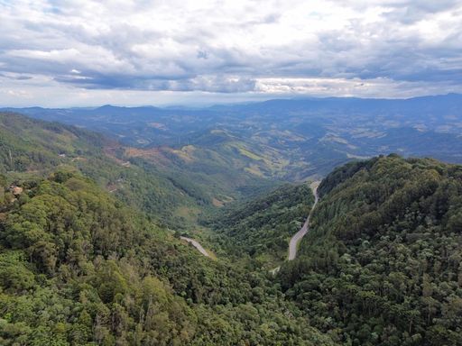 Aerial view of lush green mountains and winding road under a cloudy sky in a scenic landscape.