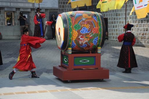 Traditional Korean drummers in colorful attire perform with a large, ornate drum at a cultural event in Seoul.