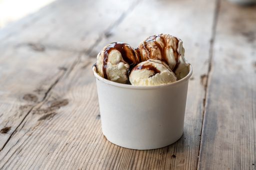 Three balls of white ice cream with caramel syrup on a rough wooden table