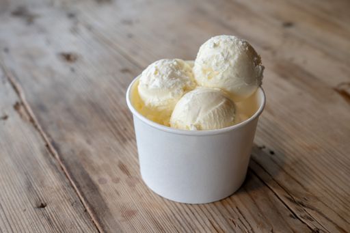 Three balls of white ice cream in a cardboard cup on a rough wooden table
