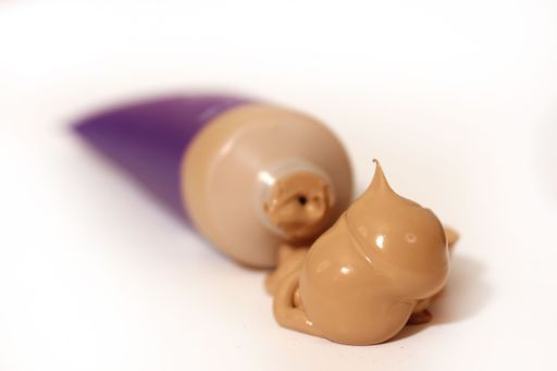 Close-up of a foundation tube with makeup cream oozing out on a white background.