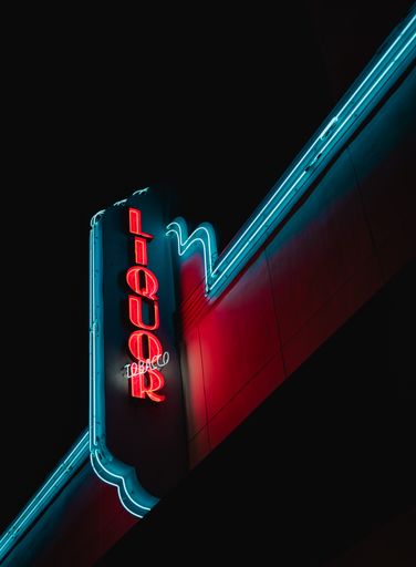 A red "Liquor" glowing red sign on a building with blue neon lights