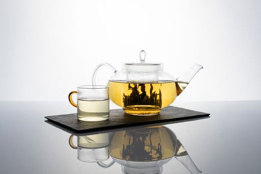 A closeup shot of tea leaves on a glass teapot against a white background