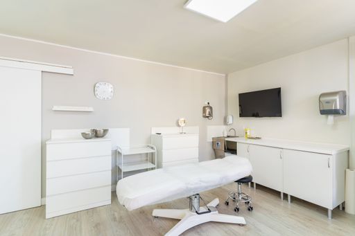 Bright medical consultation room with examination bed, clean white furniture, modern decor, and clinical equipment for professional healthcare service