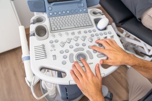 Close-up of hands using diagnostic ultrasound equipment in a clinical healthcare setting.