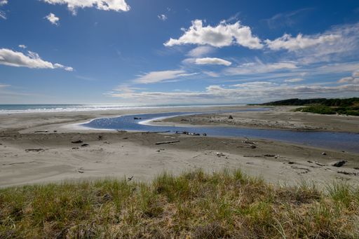 A view of The Waitohu River estuary at Otaki Beach with a winding stream under a bright blue sky and fluffy clouds.