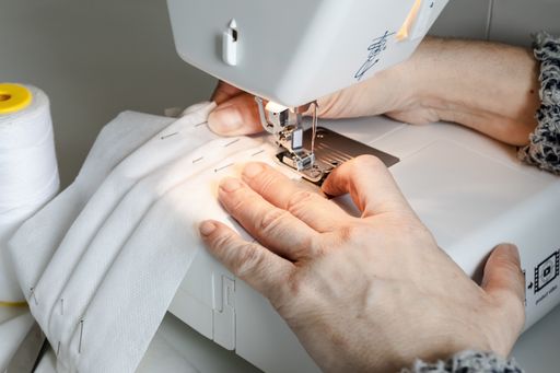 An old woman sewing face mask with the help of a sewing machine
