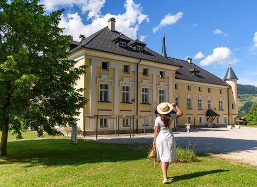 Rear view of young woman wearing white dress in park in front of beautiful Bukovje Castle in Dravograd, Slovenia