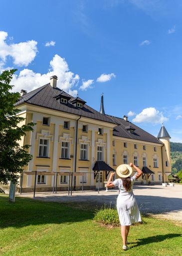 Rear view of young woman wearing white dress in park in front of beautiful Bukovje Castle in Dravograd, Slovenia