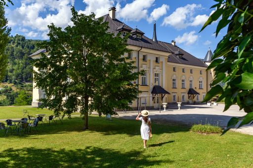 Rear view of young woman wearing white dress in park in front of beautiful Bukovje Castle in Dravograd, Slovenia