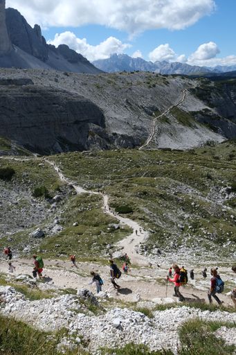 A vertical shot of a group of people hiking in the Drei Zinnen nature park under a cloudy sky in Italy