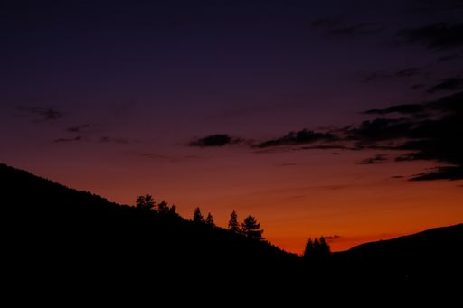A mesmerizing view of red sunset sky with the silhouettes of mountains and trees