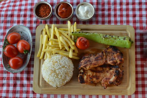 A top view of fried meat with french fries, sauces, and cooked rice on a board in a restaurant