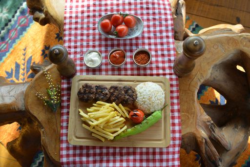 A top view of fried meat with french fries, sauces, and cooked rice on a board in a restaurant