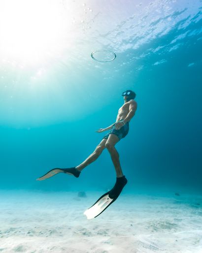 A view of a person with surfing attire underwater on a sunny day