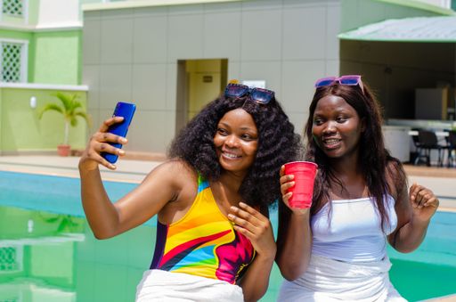 The cheerful young beautiful Nigerian females having fun by the pool and taking selfies