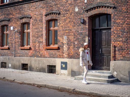 Young model wearing beige jacket and cap in front of red brick building in Katowice on a sunny winter day, Poland. High quality photo