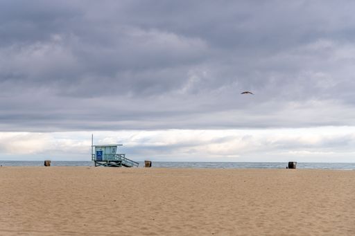 A lifeguard tower on an empty beach under a cloudy sky, with a bird flying overhead, capturing a serene coastal scene.