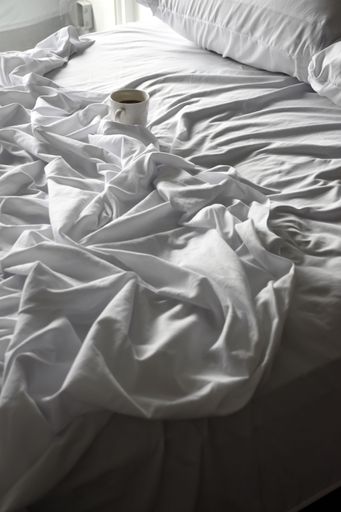 A cozy morning scene with a cup of coffee on a rumpled bed with white sheets, softly lit by natural light.