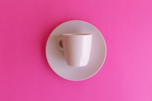 A top view of a ceramic coffee cup on a plate isolated on pink background