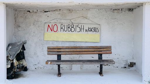 A sign saying "no rubbish" on the wall of an abandoned little shack with a wooden bench in front of it