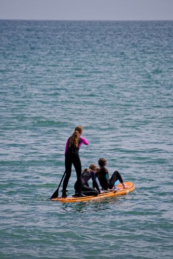 Vertical shot of three Caucasian girls on a SUP (stand up paddle boarding) on the sea on sunny summer day. Water sports in Ireland.