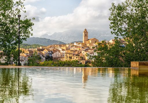 A town surrounded by a mountain range on a cloudy day reflected in the water