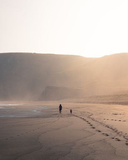 A beautiful view of a people walking on the sand near the coast with the mountains in the background