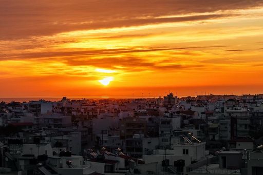 Dramatic sunset over a city skyline with vibrant orange hues and silhouetted buildings, creating a stunning urban landscape.