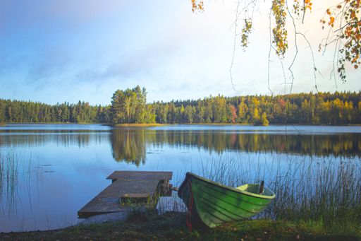 A beautiful lake surrounded by trees with a wooden dock and an old green boat in Finland