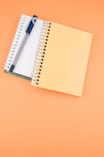A vertical shot of a notebook and a pen on an orange background - education concept