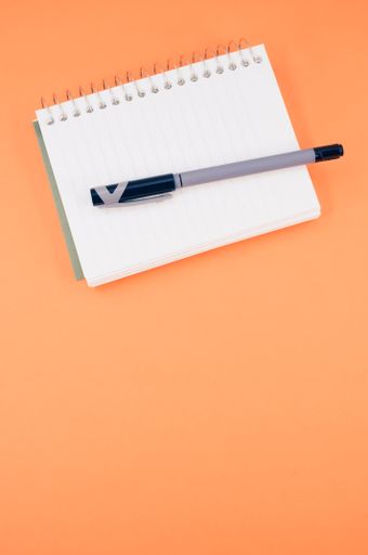 A vertical shot of a notebook and a pen on an orange background - education concept