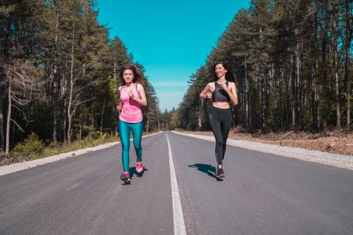 Two young slim attractive sexy happy sporty Caucasian girls jogging on the empty road in summer