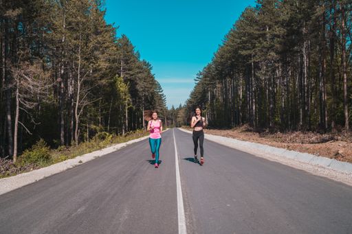 Two young slim attractive sexy happy sporty Caucasian girls jogging on the empty road in summer