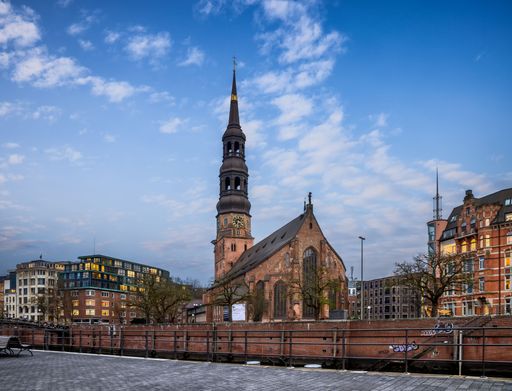 Historic St. Catherine's Church with its tall spire in Hamburg, Germany, under a partly cloudy blue sky.