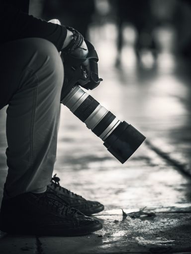 A vertical grayscale closeup of the photographer sitting in the street and holding the camera.