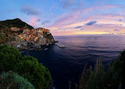 A picturesque view of Manarola, Cinque Terre at sunset with colorful houses and a vibrant sky over the Mediterranean Sea.